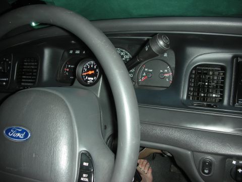 2004 Ford Crown Victoria - The interior of a Ford vehicle shows a steering wheel, dashboard, and an aftermarket tachometer gauge.