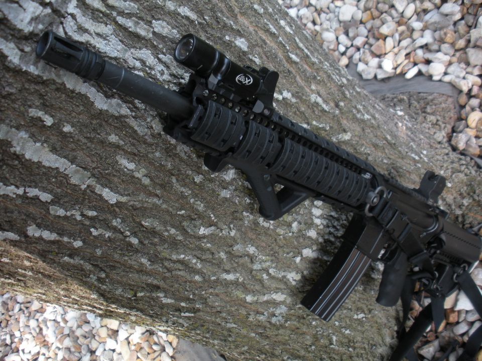 Assault rifle with scope and flashlight mounted on a tree trunk