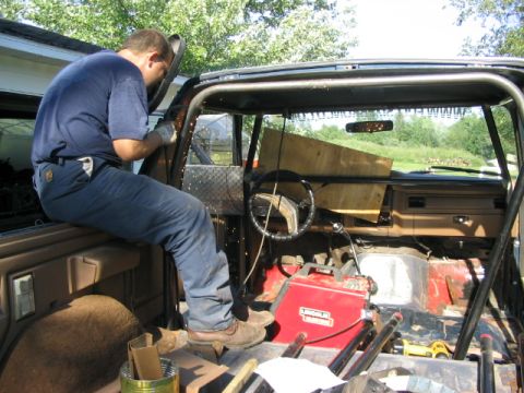 1986 Ford Bronco - A person is welding a roll cage inside a vehicle that appears to be undergoing modifications.