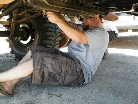 1982 Ford Bronco - Mechanics are working on the undercarriage of a vehicle, with a focus on the large tires and suspension components.