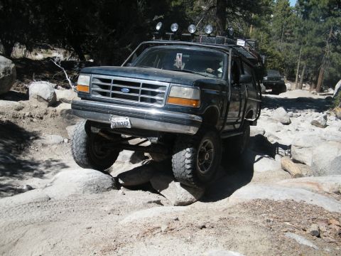 1982 Ford Bronco - This modified Ford Bronco is tackling a challenging off-road course with large rocks and uneven terrain.
