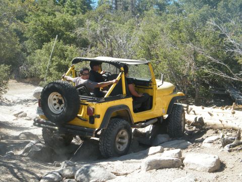 1982 Ford Bronco - A yellow Jeep Wrangler navigates a challenging rocky terrain with passengers enjoying the ride.