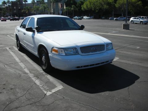 2004 Ford Crown Victoria - A white 2004 Ford Crown Victoria is parked in a cracked asphalt lot under a bright sky.