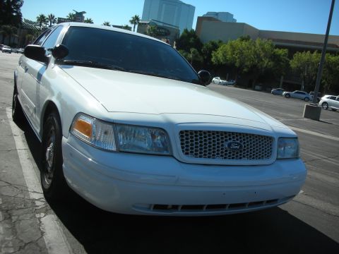 2004 Ford Crown Victoria - A white 2004 Ford Crown Victoria is parked on the side of a street with buildings in the background.
