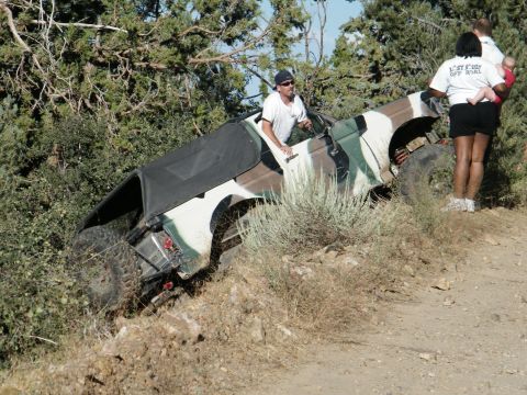 1982 Ford Bronco - A person drives an off-road vehicle with camouflage paint up a steep, dusty incline.
