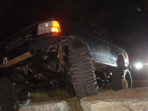1992 Ford Bronco - This black 1992 Ford Bronco is shown off-road at night, navigating large rocks with its oversized tires.