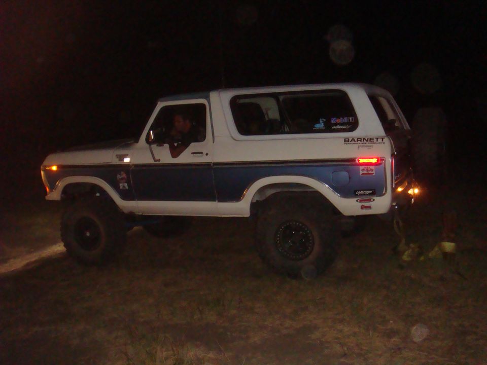 White and blue Ford Bronco with lifted suspension and off-road tires, seen from the side at night