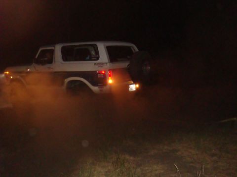 1992 Ford Bronco - Ford Bronco driving through dust at night, showing its rear-mounted spare tire and side decal.
