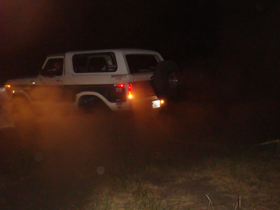 White Ford Bronco with spare tire on rear, kicking up dust at night. Barnet decal visible on side