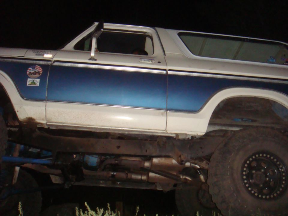 Side view of a lifted Ford Bronco with blue and white paint, showing aftermarket wheels and exhaust