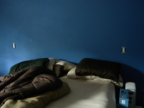 1992 Ford Bronco - A messy bed with blankets and pillows is shown against a blue wall with light switches.