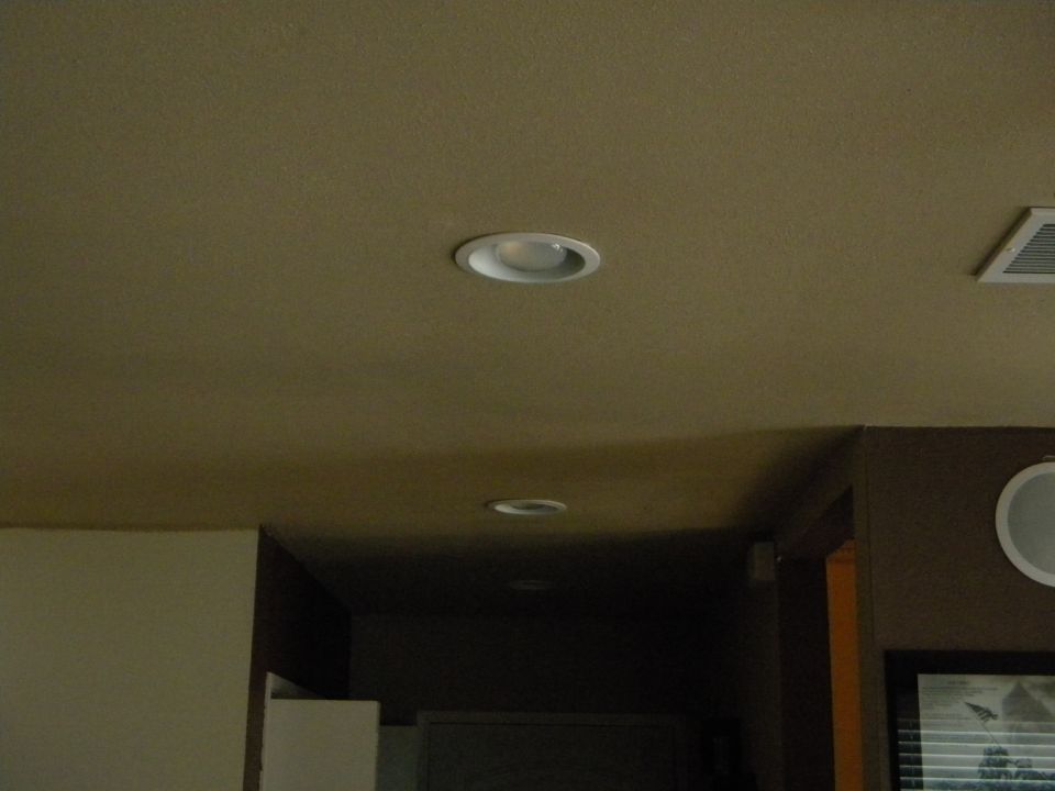 Ceiling with recessed lights and an air vent, with a partial view of a wall and a framed picture