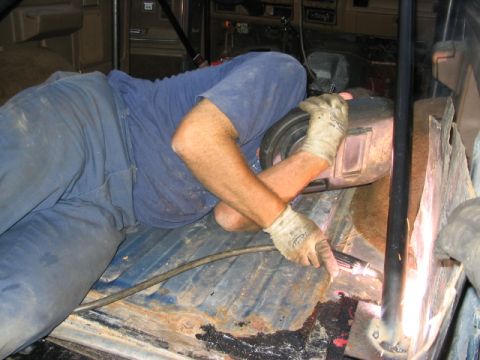 1986 Ford Bronco - A person in a welding mask works on the interior floor of a vehicle.