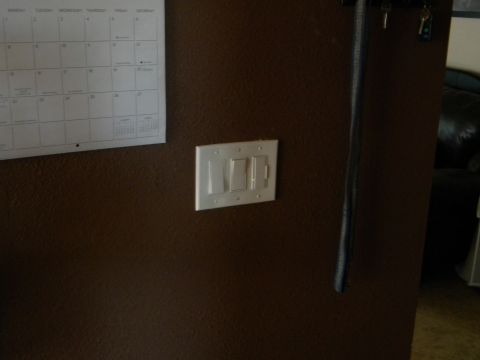 1992 Ford Bronco - A calendar hangs on the wall above a set of light switches, with a dark object to the right.