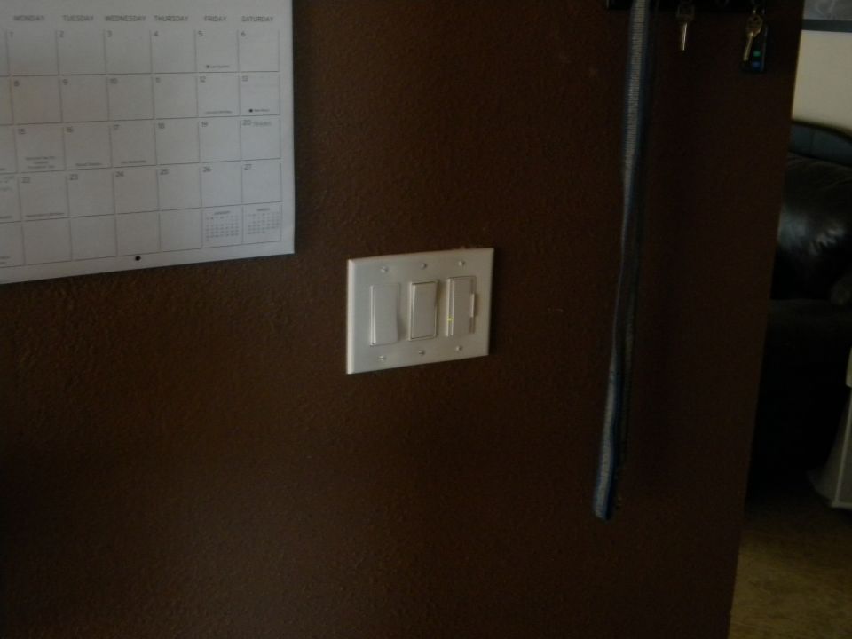 Light switches on a brown wall next to a calendar. A dark object hangs vertically on the right