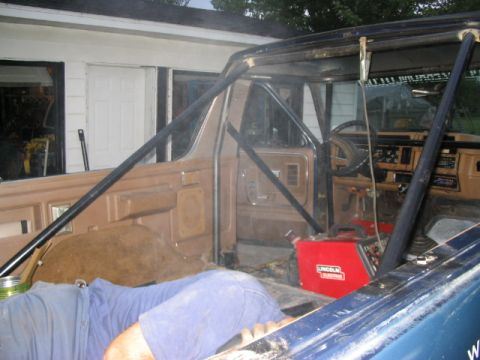 1986 Ford Bronco - The interior of a Ford Bronco shows a custom roll cage installation, with a welding machine visible in the cargo area.