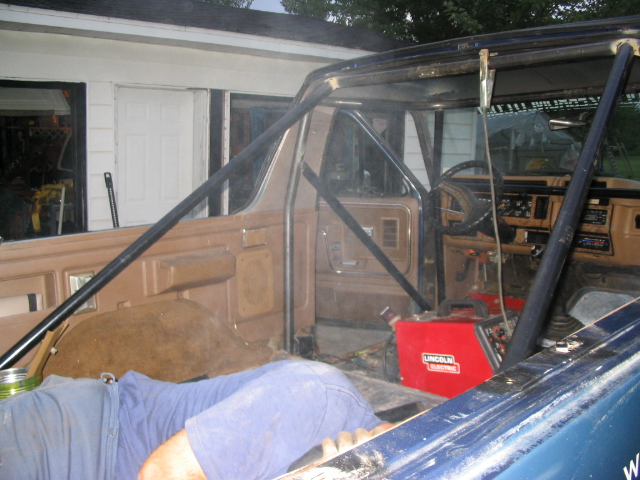 Ford Bronco interior with bare-metal roll cage under construction, welder inside