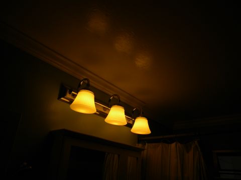 1992 Ford Bronco - A row of three illuminated vanity lights with yellow glass shades is mounted above a mirror.