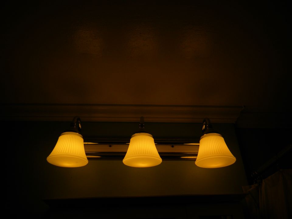 Three yellow pleated lamps hang from a fixture above a dark wall
