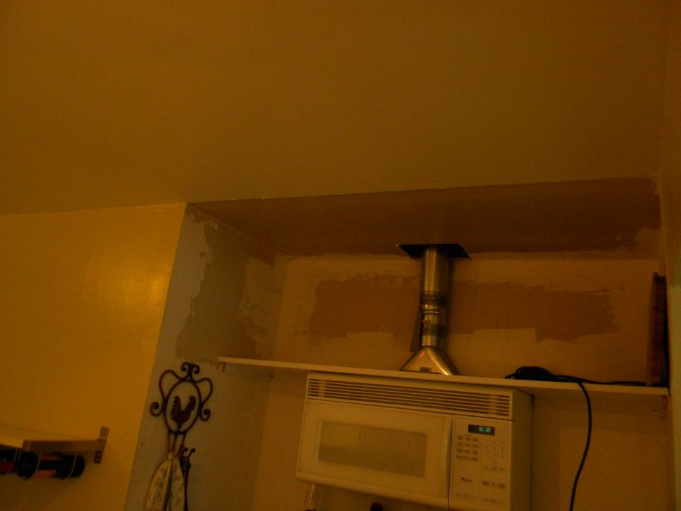 Microwave oven on a shelf with a metal vent pipe above it