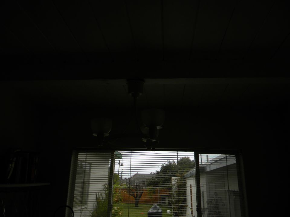 Interior of a dark room looking out a sliding glass door to a backyard