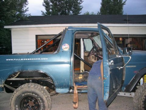 1986 Ford Bronco - Blue Ford Bronco with interior roll cage and website text on the exterior.