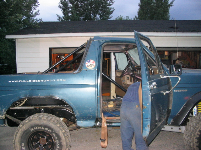 Blue full-size Ford Bronco with top off and roll cage exposed, door open, black fender flares