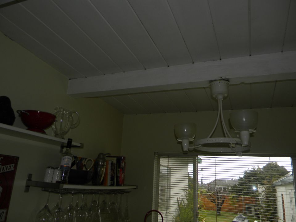 Interior scene with white paneled ceiling, shelves holding glassware and bowls, and a window showing houses and trees