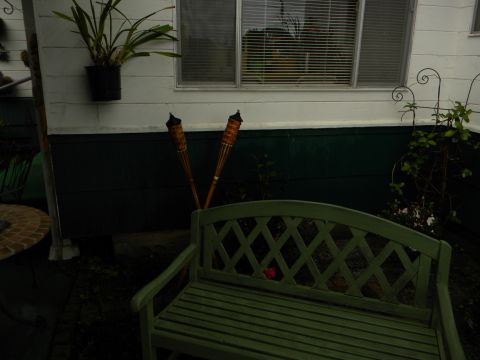 1992 Ford Bronco - A green wooden bench sits on a patio next to tiki torches, with a potted plant above a window.
