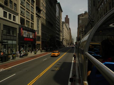 1992 Ford Bronco - A yellow taxi cab navigates a busy city street, with tall buildings lining both sides.