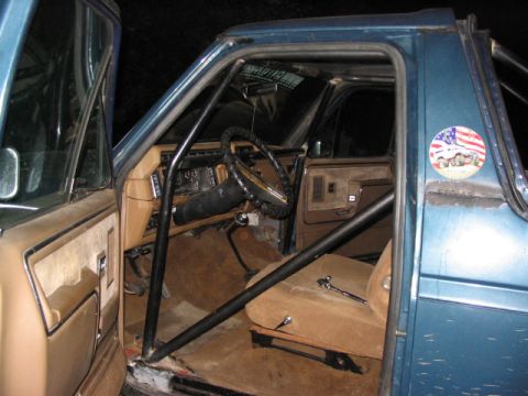 1986 Ford Bronco - The interior of a blue SUV is visible, a roll cage and tan upholstery.