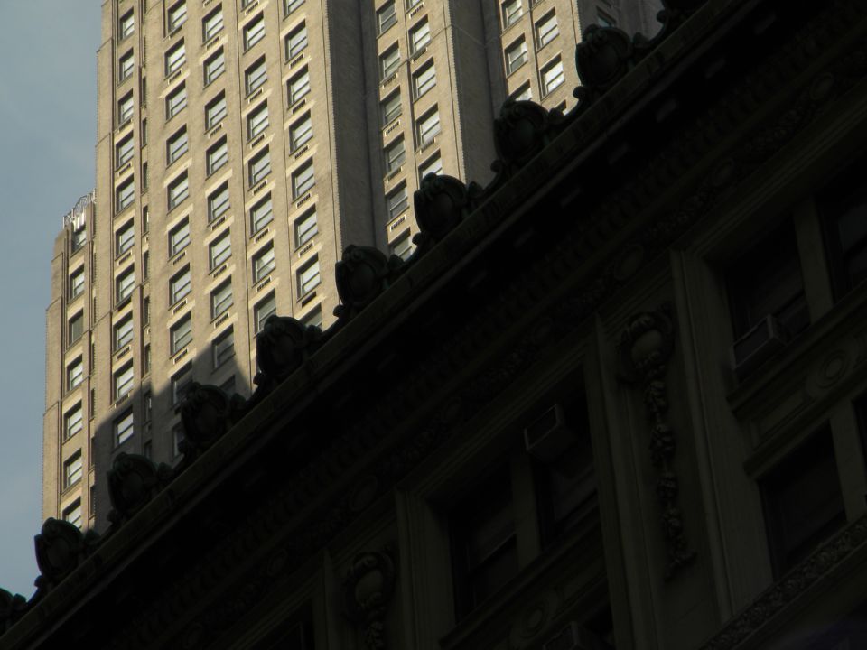Two tall buildings, one in shadow, with ornate architectural details on the lower one