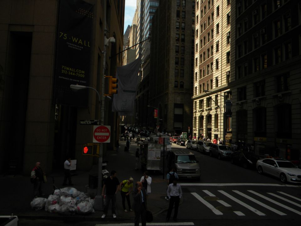 New York City street with tall buildings, traffic, and pedestrians. A banner for 75 Wall Street is visible