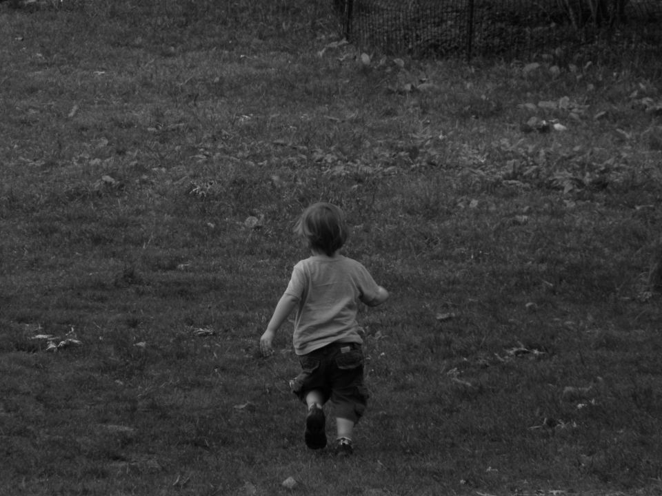 Child running away from camera across a grassy field