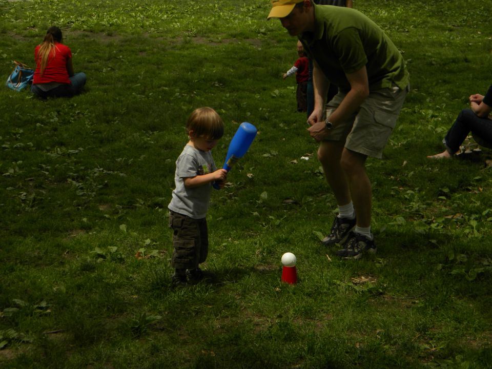 Child swings blue bat at tee-ball, adult watches