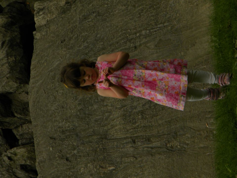 Young girl in a pink floral dress standing near a large rock formation