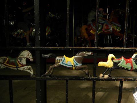 1992 Ford Bronco - A row of carousel horses are visible behind a dark fence, with blurred figures on a carousel in the background.