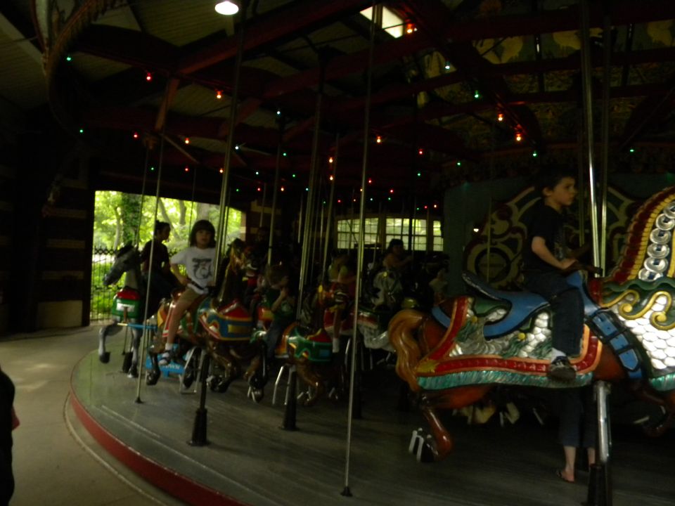 Children ride painted horses on a carousel inside a building with lights