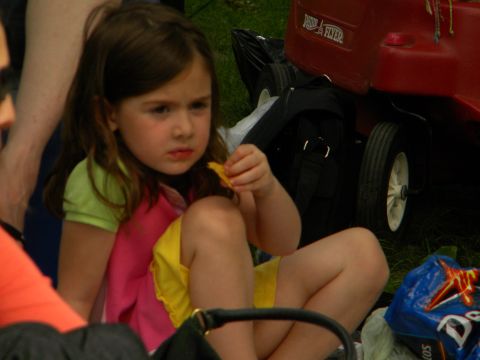 1992 Ford Bronco - A young girl sits on the grass, looking away from the camera while holding a snack, with a red wagon in the background.
