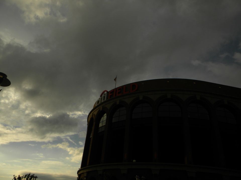 Exterior of a stadium with "FIELD" visible on top, under a cloudy sky. Watermark says SUPERMOTORS