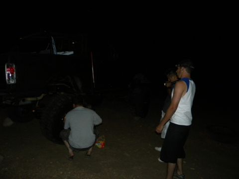 1992 Ford Bronco - A group of people are gathered around a large vehicle at night, with one person appearing to work on a tire.