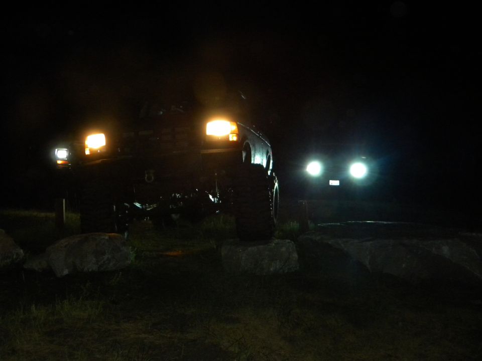 two SUVs with headlights on at night, one in foreground, one in background