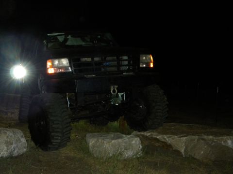 1992 Ford Bronco - A black 1992 Ford Bronco is shown on rocks at night, illuminated by its headlights.