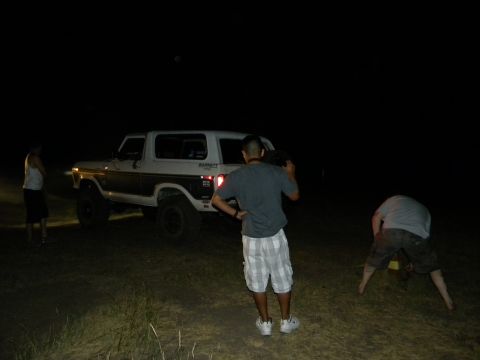 1992 Ford Bronco - A white and brown Ford Bronco is visible at night with several people around it.