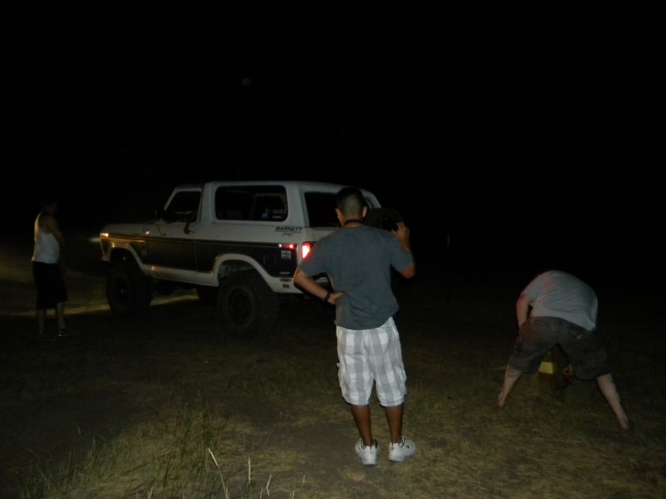 White and brown Ford Bronco with aftermarket wheels, seen at night from a 3/4 front angle