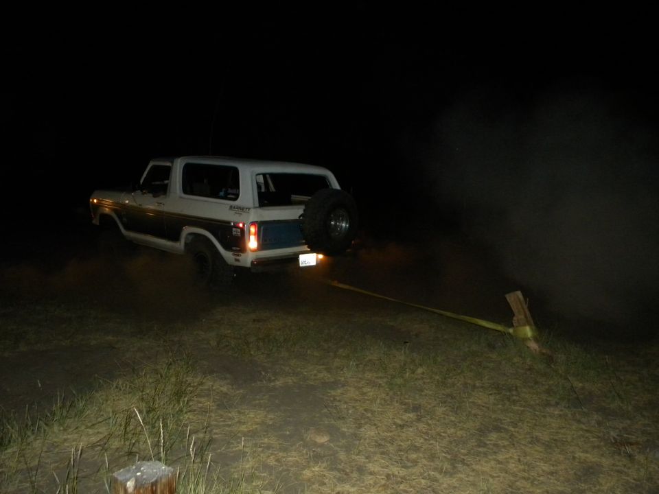 Ford Bronco with spare tire on back, being towed by a strap at night