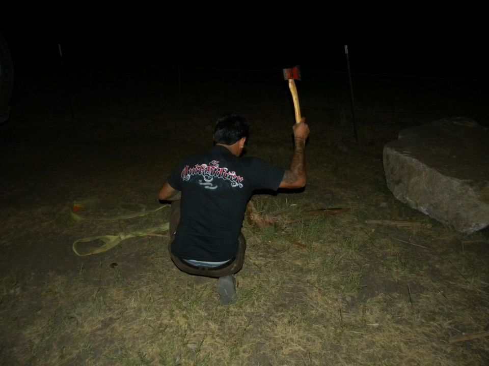 Man crouched in dark holding an axe, with a large rock to the right