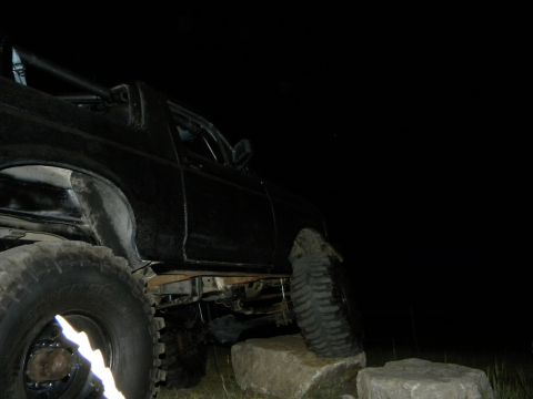 1992 Ford Bronco - This modified SUV is positioned on rocks, with its large tires visible against the dark background.