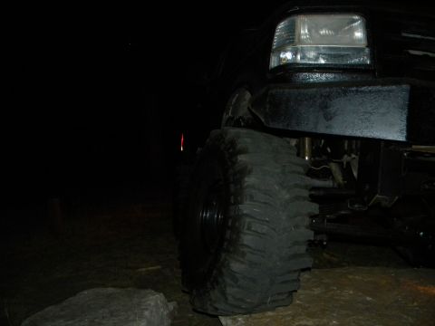 1992 Ford Bronco - A close-up view of a black SUV's front tire and headlight, captured in the dark.