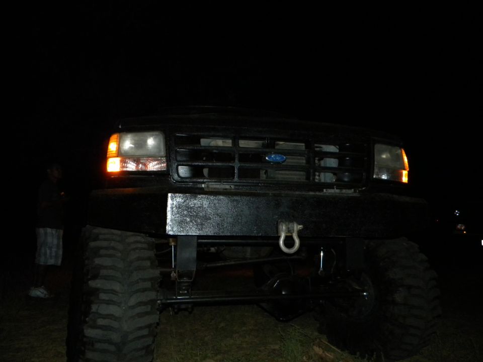 Front view of a black Ford F-Series truck with a custom bumper and large tires at night